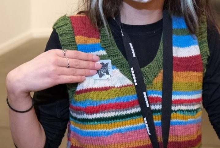 A figure from the neck down, putting a sticker on a colorful striped vest.