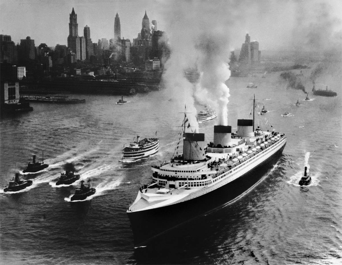 A black and white photograph of a ship with 3 funnels moving away from the New York City skyline.