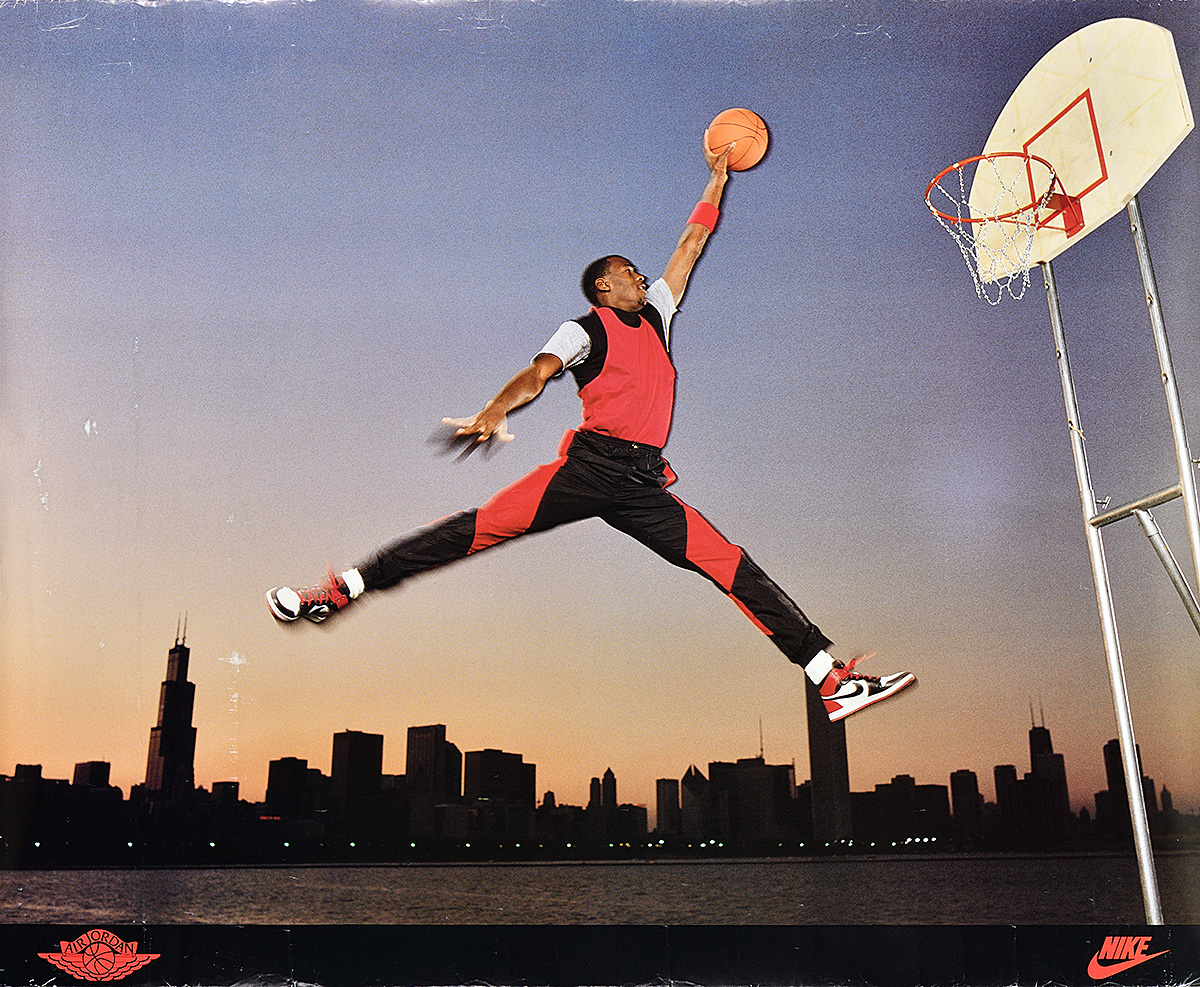 A poster of a Black man in front of a cityscape, legs splayed as he leaps to dunk a basketball.