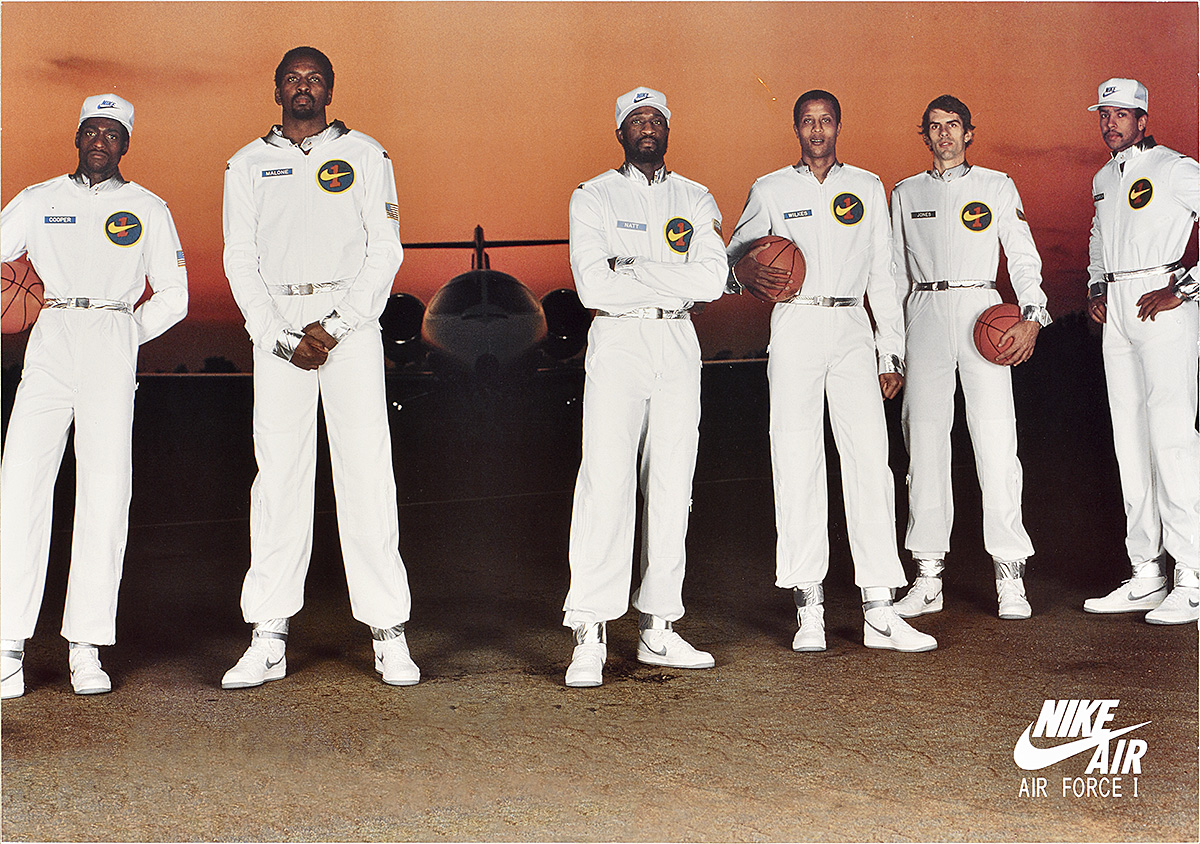 A poster of 6 tall men wearing white flight suits and Nike shoes in front of a helicopter.