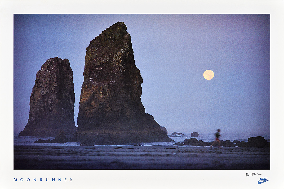 A poster of a blurry figure running along a beach on a moonlit night past 2 large rock formations.