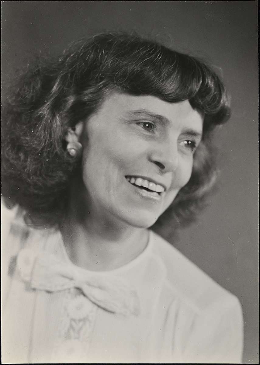A black and white photograph of a middle aged white woman with short hair looking to the side and smiling.