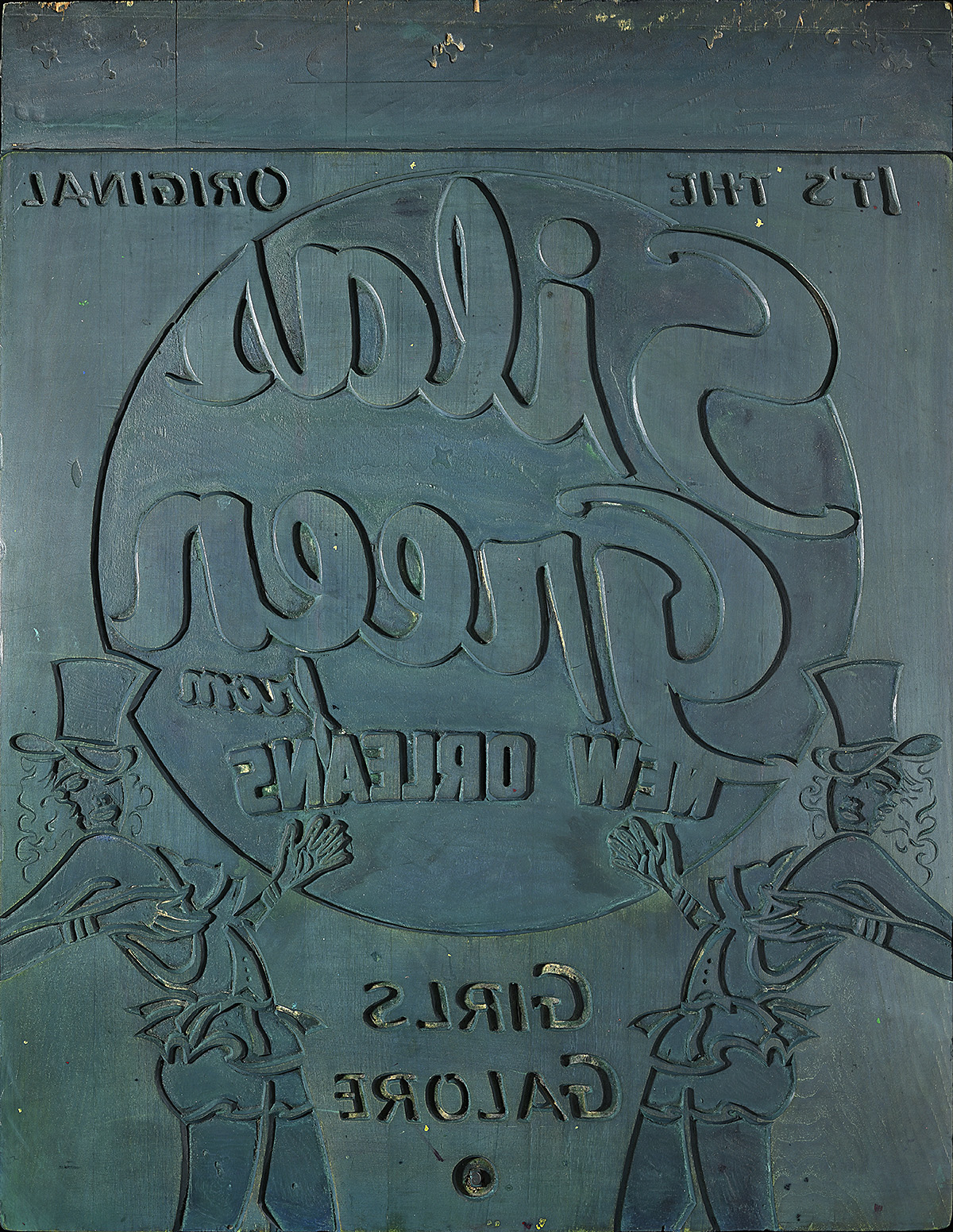 A green toned printing block with two dancing women and backward text.