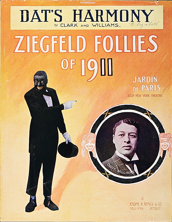 A Black man in a suit pointing to a circle enclosing a black and white photograph of a young man's face.